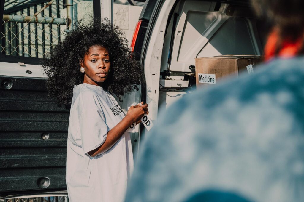 A woman assists with unloading medicine boxes from a van for a community charity event.